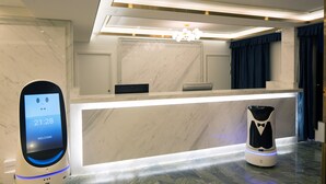 A hotel reception area with a marble counter, a digital clock displaying 21:28, and a robot. - Livington Hotel (Vallingby)