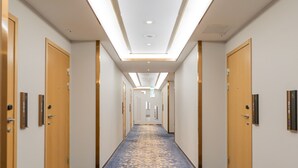A hotel hallway with a blue carpet, wooden doors, and a ceiling light fixture. - Livington Hotel (Vallingby)