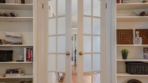 Una habitación con una puerta blanca grande, estanterías con libros y objetos decorativos, y una cesta de mimbre a la derecha.