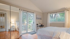 Un dormitorio con una cama grande, un ventanal corredero que da a un balcón, una mesita de noche pequeña y una mesita auxiliar.