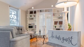 Una sala de estar con un sofá gris, una mesa de centro de madera y un cartel que dice 'be our guest'.