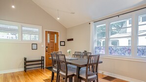 Un comedor con mesa y sillas de madera, un banco y un ventanal con vistas a árboles y casas.
