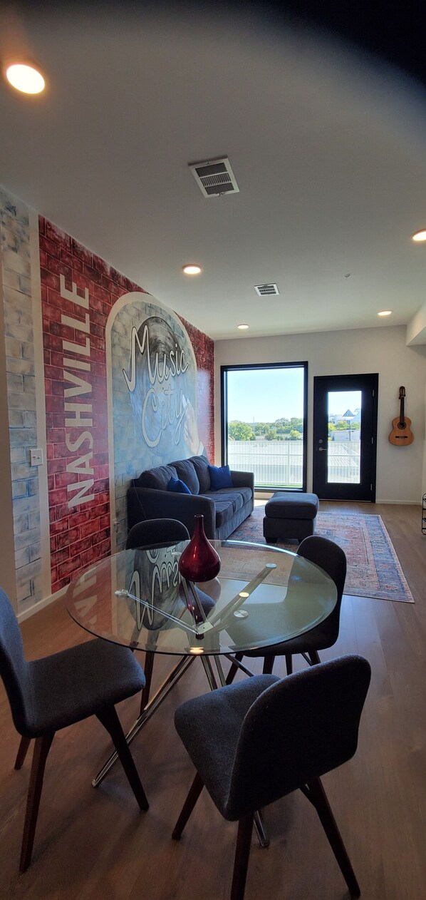 A modern living room with a glass coffee table, dark sofas, and a red vase. A mural on the wall reads "Music City." - Walk! Gulch,Honkeytonks,Music Row, Nashvilles Best Location ! (Nashville)