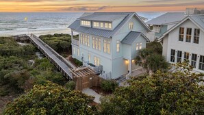 Een huis aan de kust met een terras met uitzicht op de oceaan, een houten hek en weelderige begroeiing.