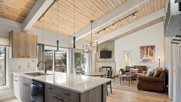 A modern kitchen with a large island, wooden ceiling, and a dining area with a fireplace.