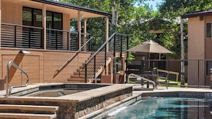 A swimming pool with steps leading into it, a covered seating area, and a building with a wooden facade and a staircase.