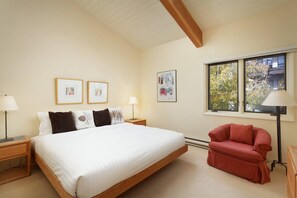 Ein Schlafzimmer mit einem Bett, zwei Nachttischen, einem roten Sessel und zwei gerahmten Bildern an der Wand.