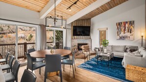 A spacious living area with a large wooden ceiling, a fireplace, a television, and a dining area with a round table and chairs.