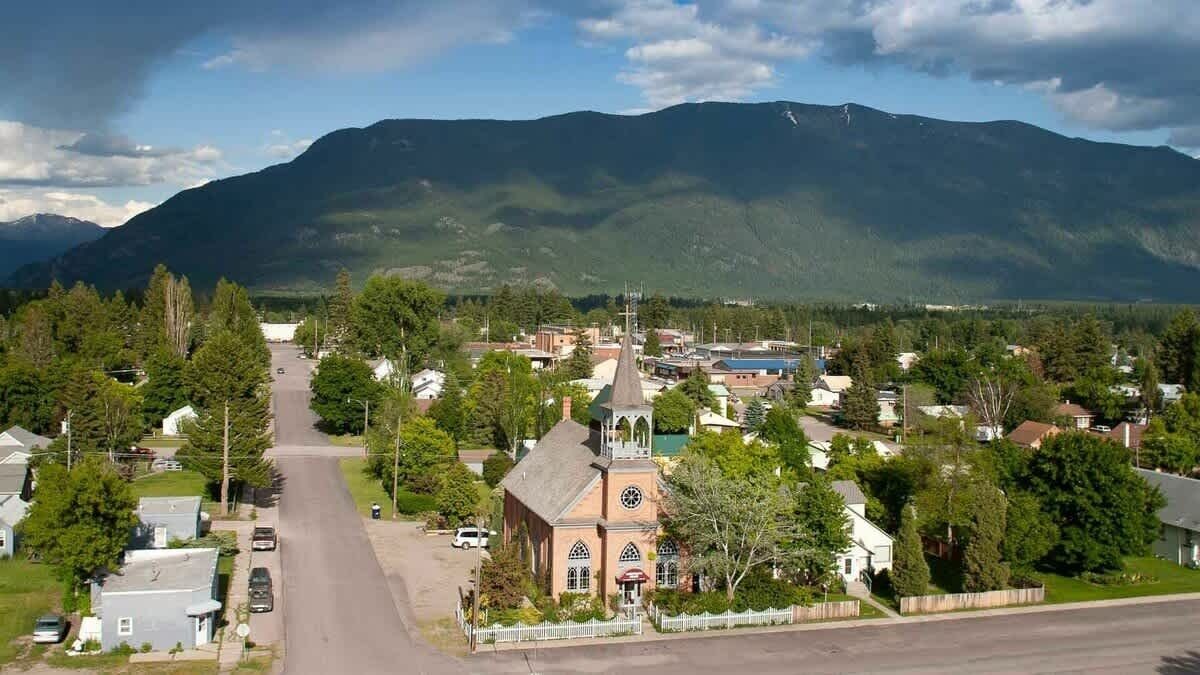 Un pueblo con una iglesia destacada, una calle principal y montañas al fondo.