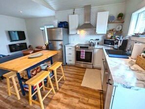 Une cuisine compacte avec une table en bois, deux tabourets, un four à micro-ondes, un four traditionnel et un évier.
