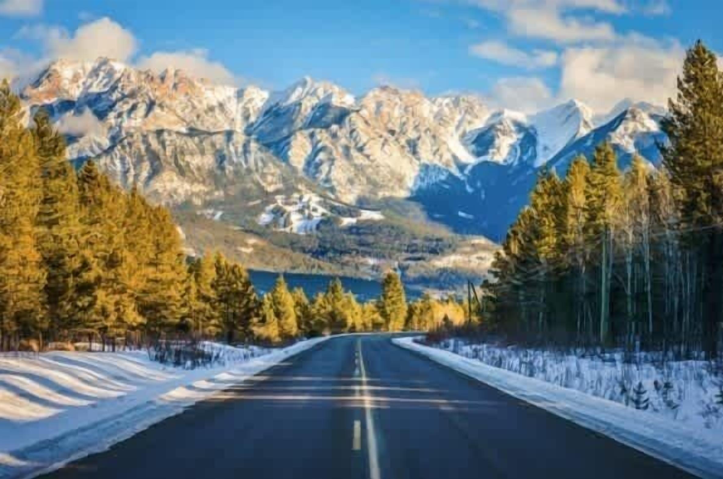 Une route menant à un paysage montagneux, avec un sol et des arbres couverts de neige.