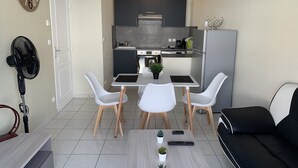 Ett kompakt bostadsutrymme med ett litet kök, en matplats med bord och stolar, en soffa och en fläkt.