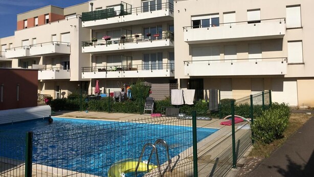En modern lägenhetsbyggnad med en swimmingpool, balkonger och ett inhägnat utomhusområde.