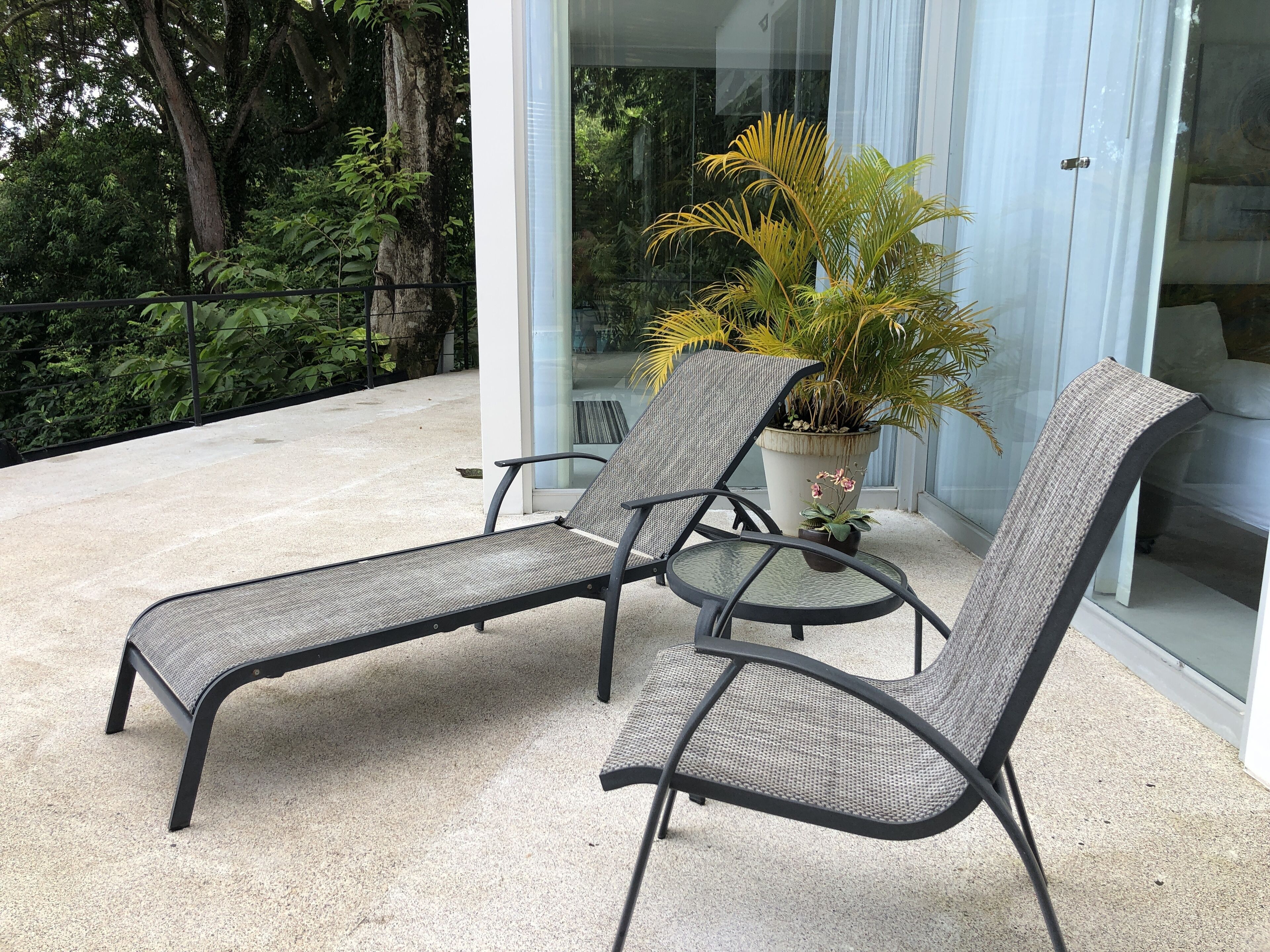 Een balkon met twee loungestoelen, een plant in pot en een glazen deur naar een kamer.