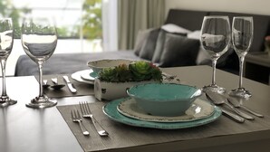 Une table à manger dressée avec des assiettes, des bols, des couverts et des verres à vin, offrant une vue sur l’extérieur.