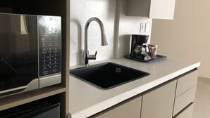 Une cuisine moderne équipée d’un four à micro-ondes encastré, d’un évier en acier inoxydable et d’une machine à café posée sur le plan de travail.