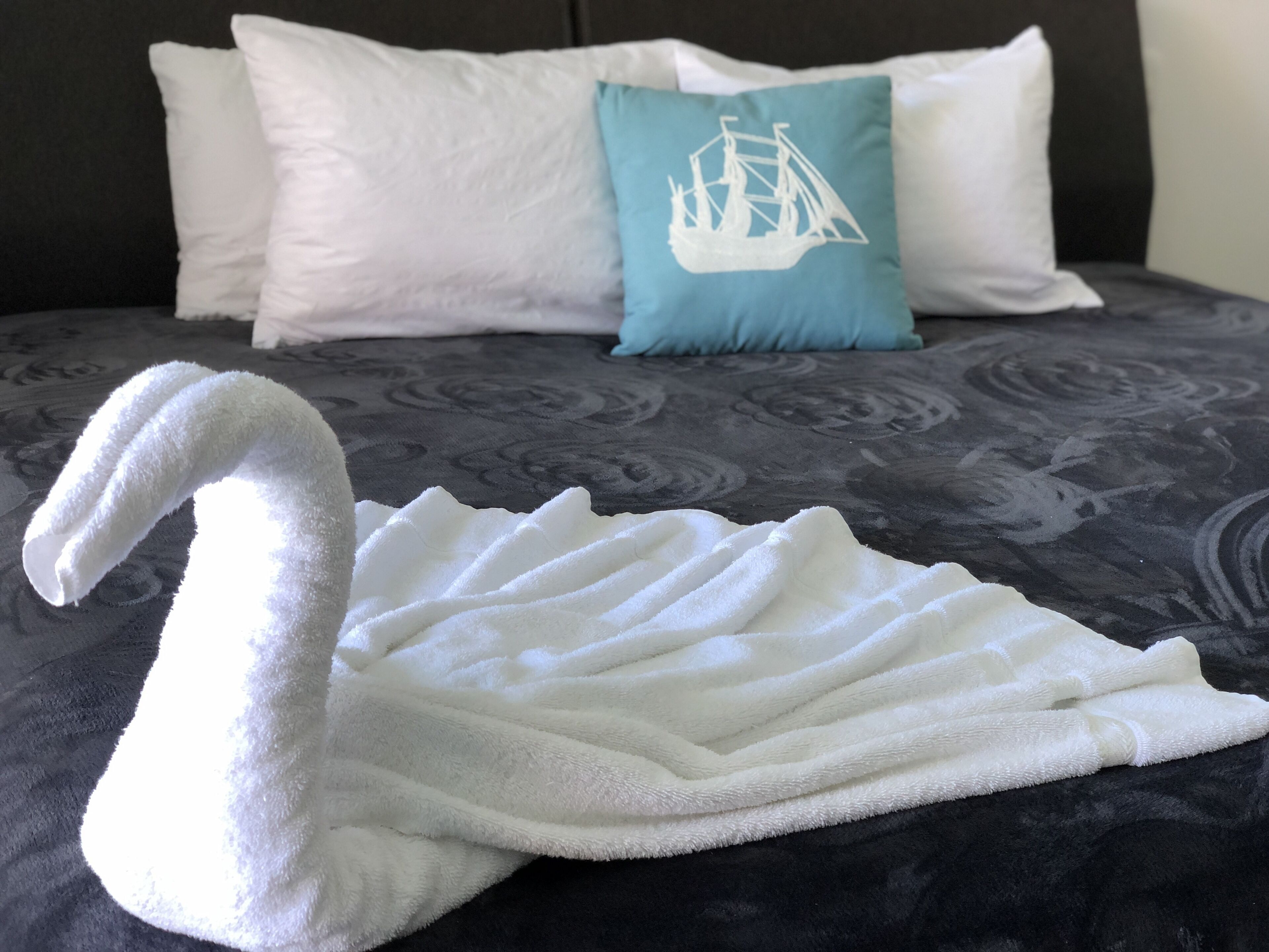 A bed with a white swan towel and a pillow with a ship design.