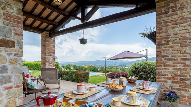 An outdoor dining area with a view of the countryside, a table set with plates, cups, and a coffee pot. - San Rocco 4, Emma Villas (Montecchio)