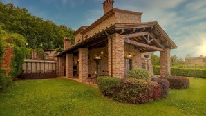 A rustic stone house with a wooden porch, surrounded by well-maintained grass and shrubs. - San Rocco 4, Emma Villas (Montecchio)