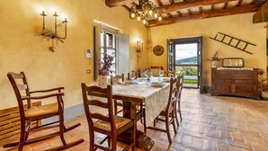 A dining area with a long table set for six, wooden chairs, a chandelier, and a view through an open door. - San Rocco 4, Emma Villas (Montecchio)