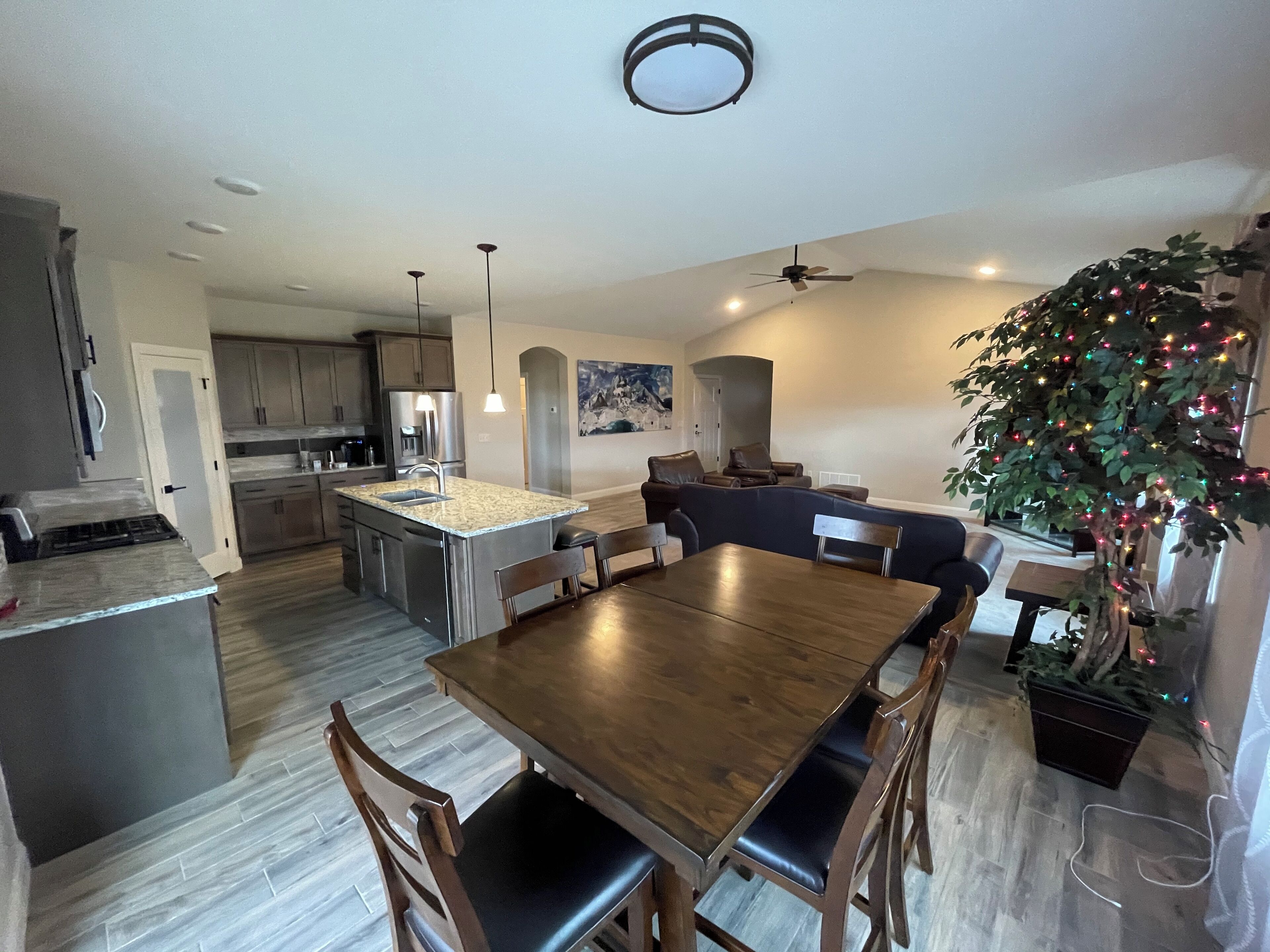Une cuisine moderne dotée d’un îlot central, un coin repas avec une table et des chaises en bois, et un espace salon avec un canapé et un sapin de Noël.