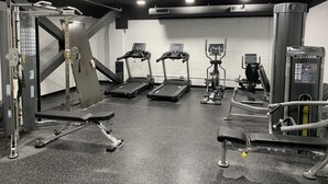 Une salle de sport équipée de tapis de course, d’une machine de musculation et d’un banc de développé couché.