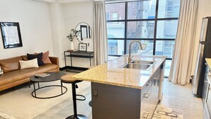 Une cuisine moderne dotée d’un plan de travail en granit, d’un évier en acier inoxydable et offrant une vue sur la ville grâce à de grandes fenêtres.