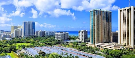 A high-rise building complex with a parking area and lush greenery.