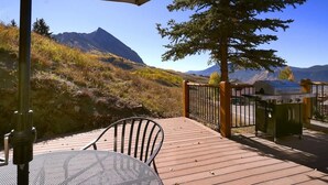 Una terraza de madera con una parrilla, una mesa y una silla, con vista a un paisaje montañoso.