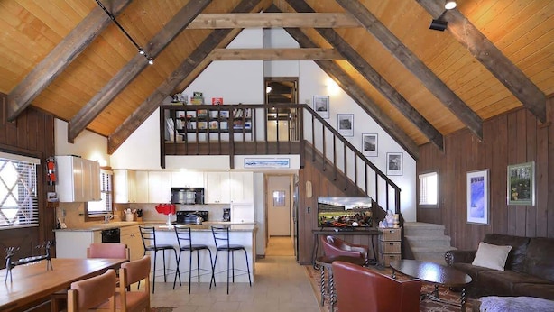 Amplia zona de estar estilo loft con cocina, comedor y escalera que lleva a un dormitorio en lo alto.