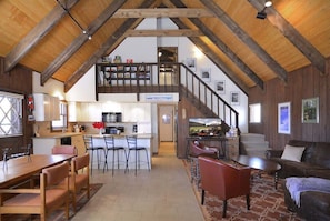 A spacious loft-style living area with a kitchen, dining area, and a staircase leading to a lofted bedroom.