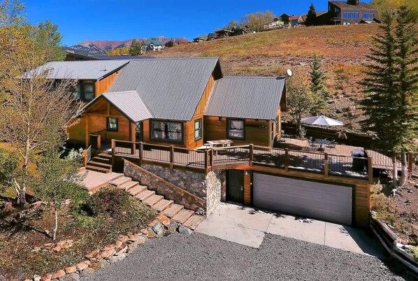 A two-story cabin with a stone staircase, a covered patio, and a garage.