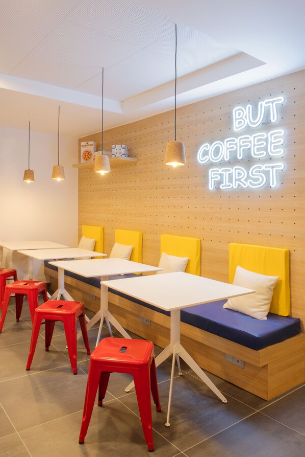 A modern cafe interior with wooden walls, neon signage, yellow cushioned seating, and red stools.