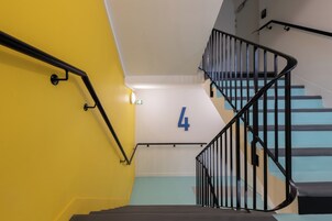 Una escalera con barandilla negra, pared amarilla y piso azul.