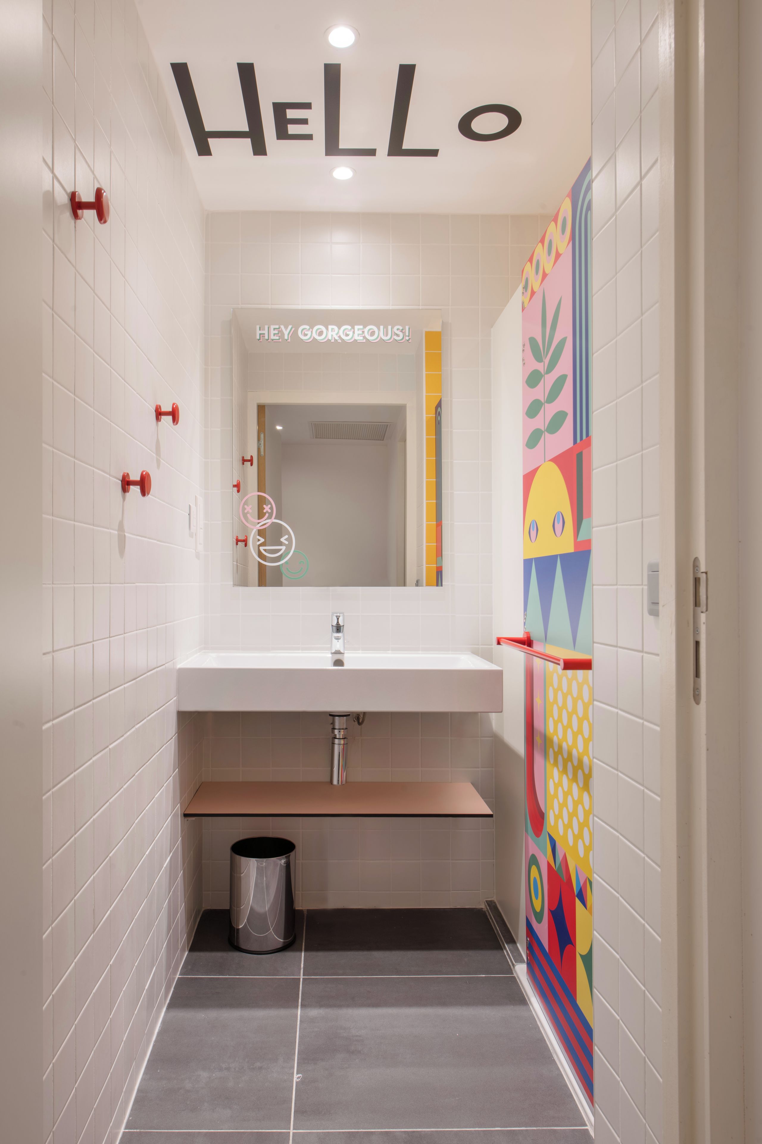 A bathroom with a white sink, a mirror, and a colorful wall decoration.