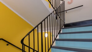 A staircase with black railings and light blue steps, leading to a landing with a white wall and a number '5' sign. - Hostel HOSHO Paris Sud Porte d'Italie (Le Kremlin-Bicetre)