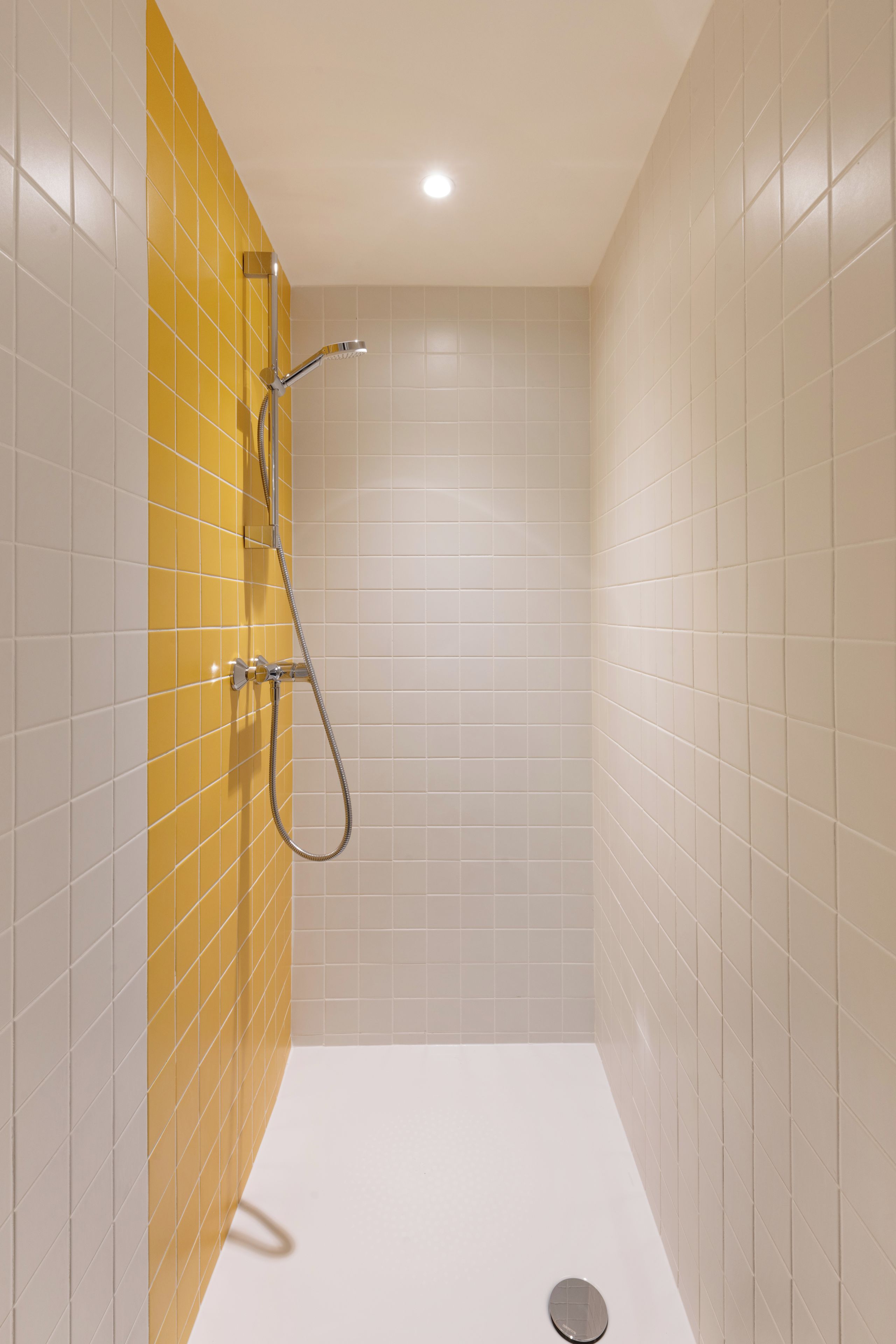 A small, enclosed shower area with a yellow accent wall and a white tiled floor.