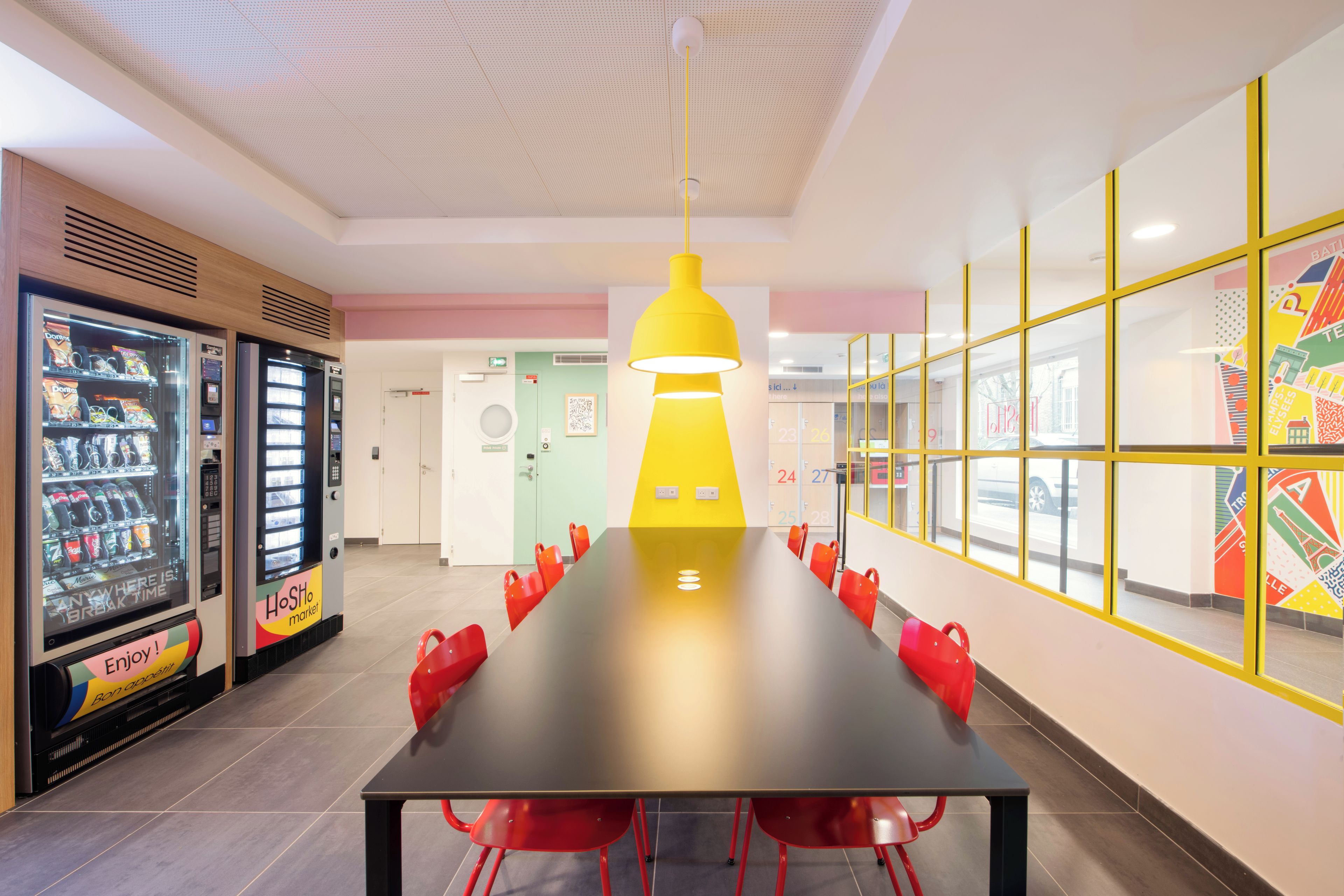 A conference room with a long table and red chairs, a vending machine, and a yellow pendant light.