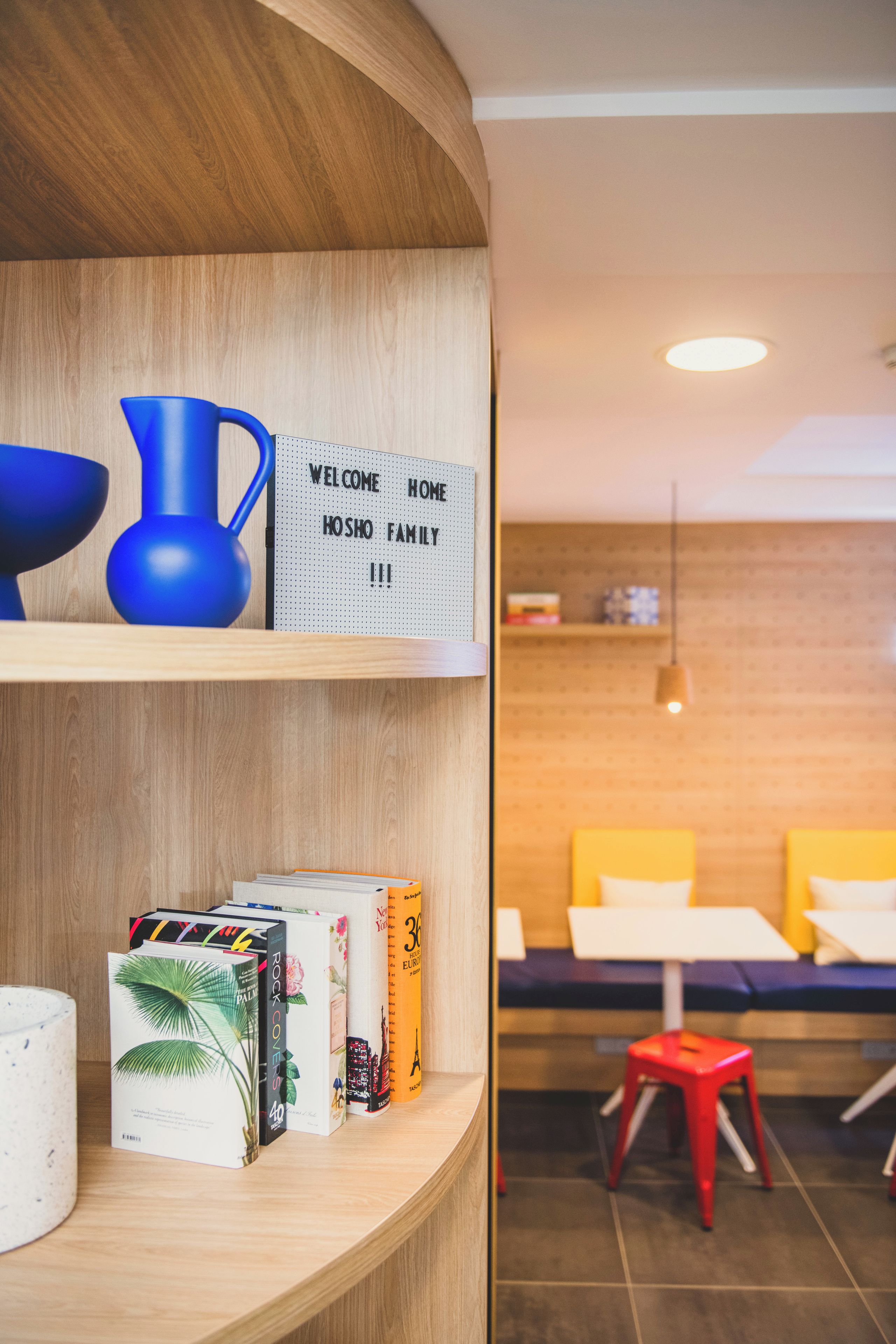 Een hotel receptie met een houten balie, een bord met welkomstboodschap en een zithoek met gele kussens.