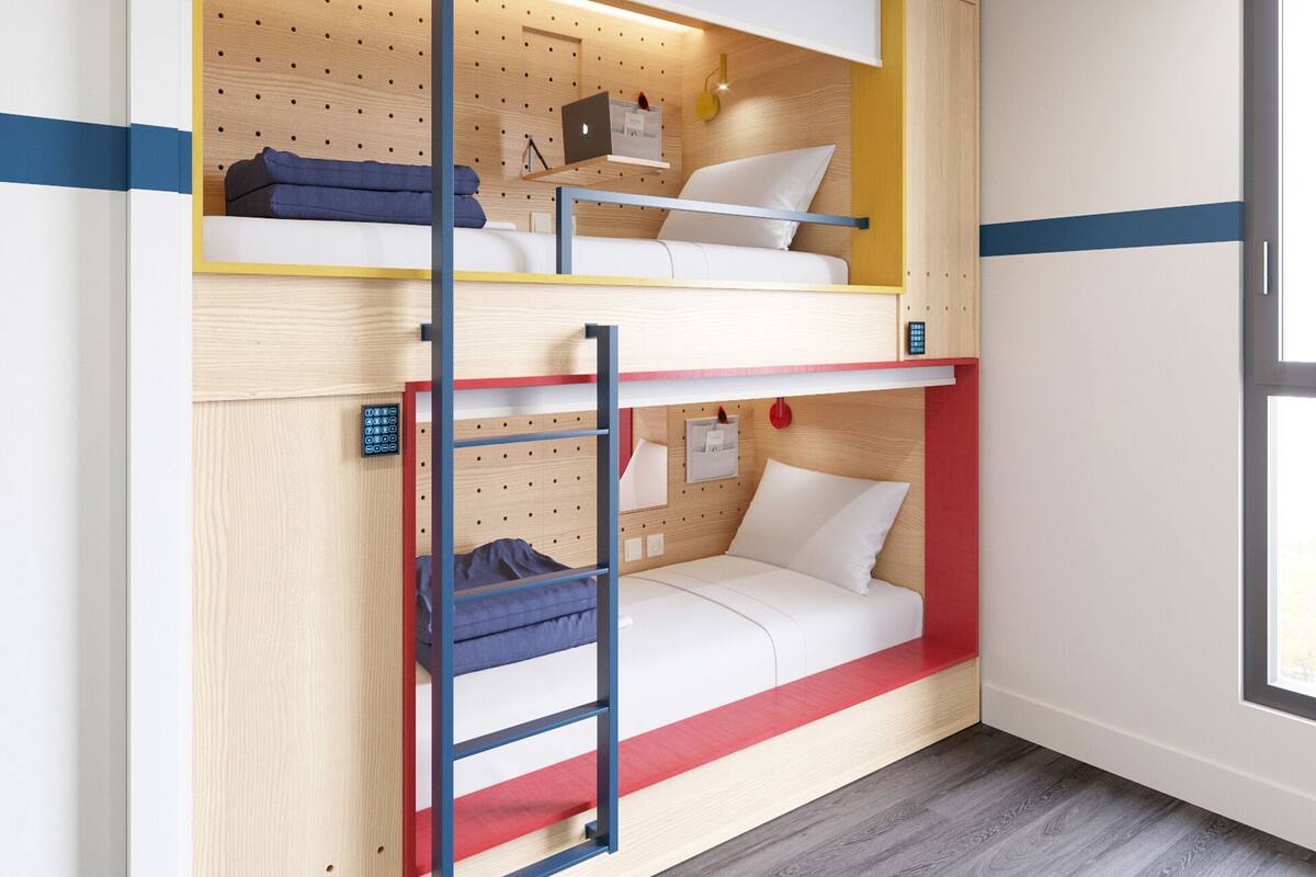 Ein Schlafraum mit Etagenbetten, einer Treppe, einem Schreibtisch mit Laptop und einem Fenster.
