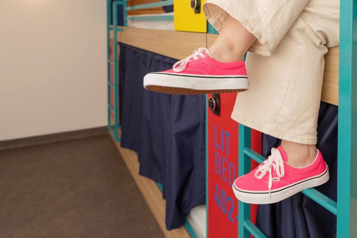 Ein Schlafraum mit Etagenbetten, eine Person sitzt im oberen Bett und trägt rosafarbene Turnschuhe.