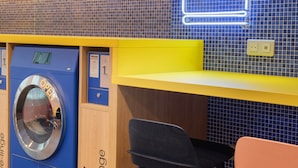A laundry facility with a blue washing machine, a neon sign reading "LAUNDRY", and a yellow counter. - Hostel HOSHO Paris Sud Porte d'Italie (Le Kremlin-Bicetre)