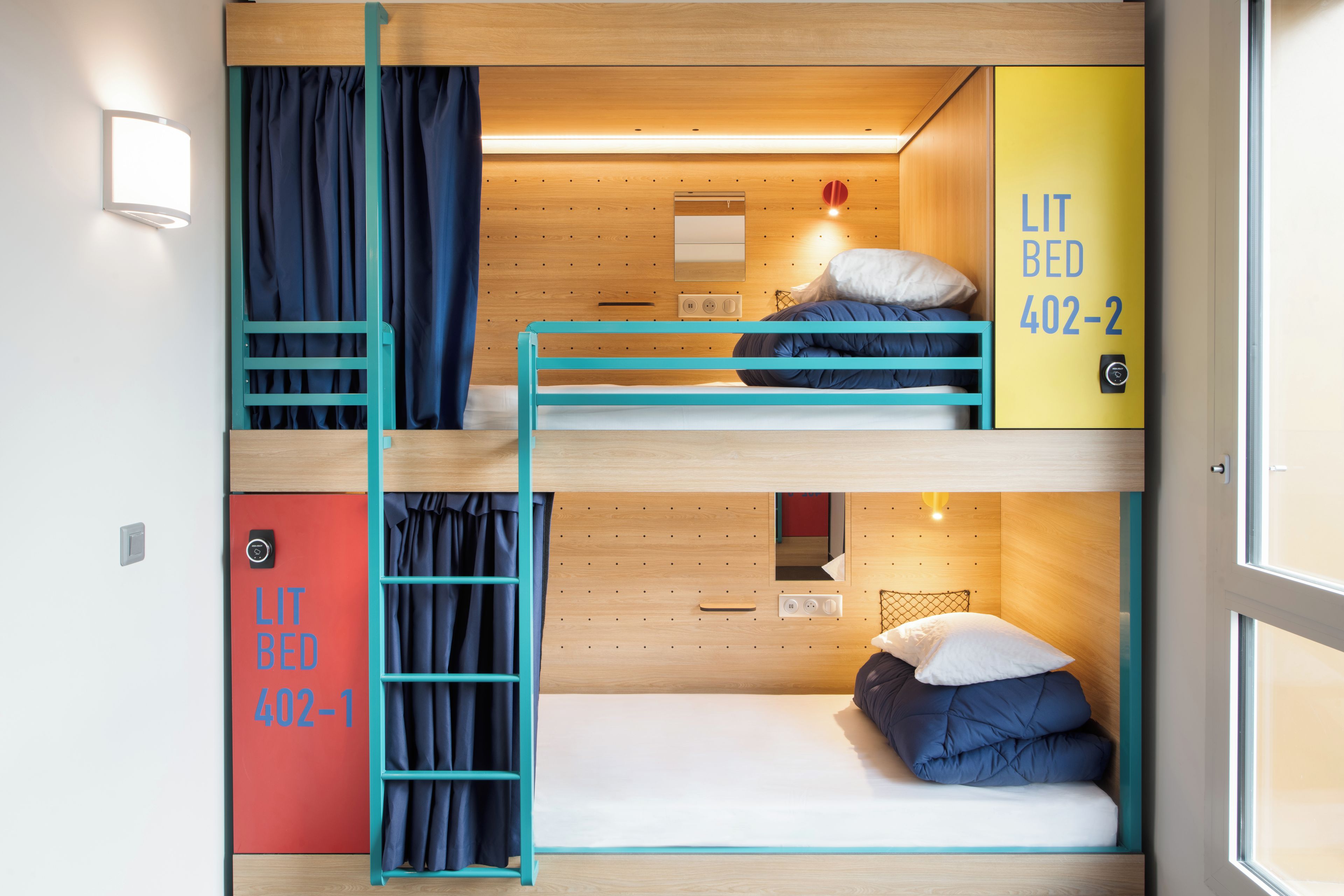 A bunk bed room with a ladder, a desk, and a bed with pillows. There are two doors, one red and one yellow, with numbers on them.