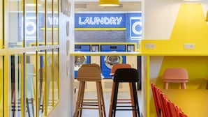 A hallway with yellow and white walls, a 'Laundry' sign, and a seating area with stools and chairs. - Hostel HOSHO Paris Sud Porte d'Italie (Le Kremlin-Bicetre)