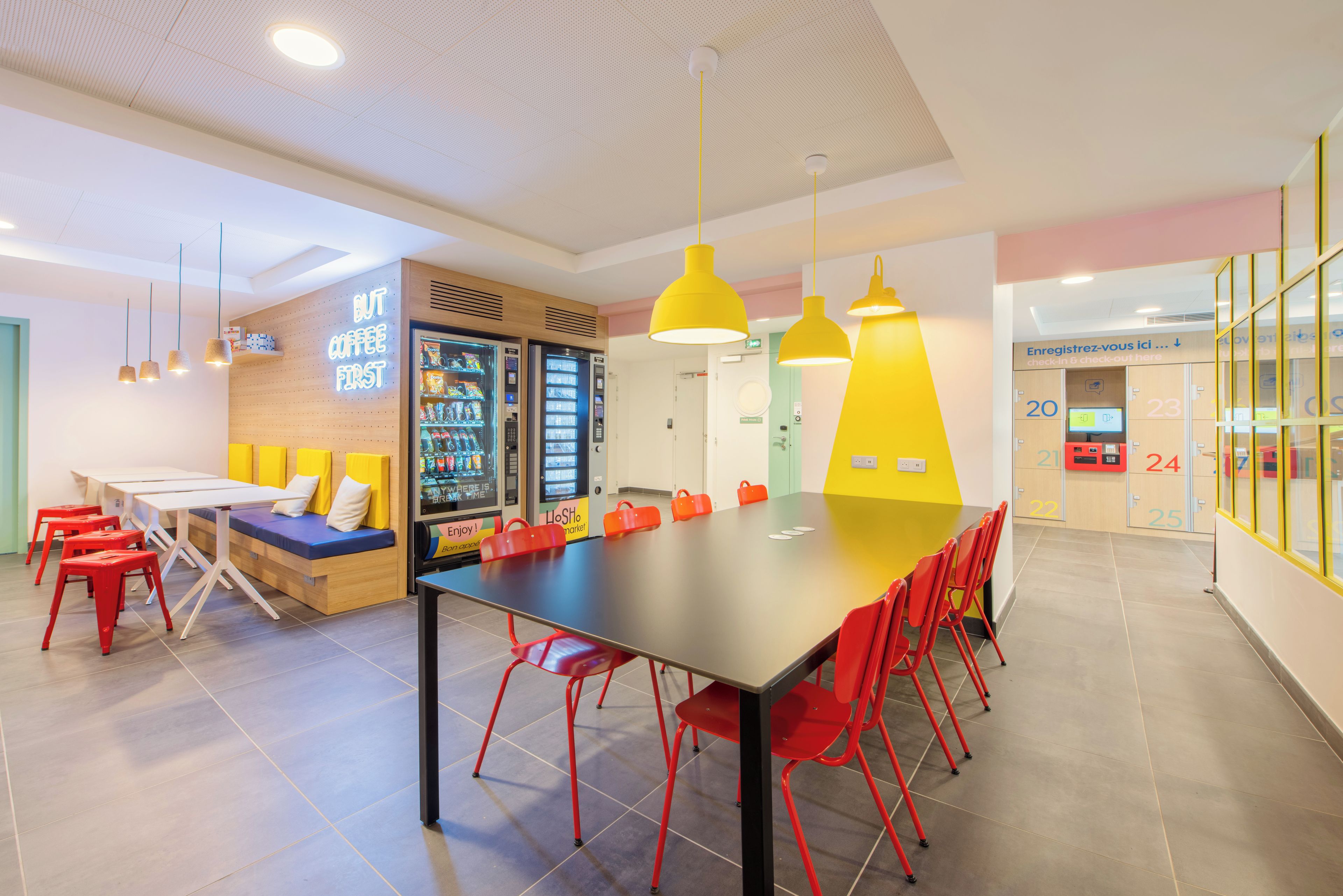 A modern interior with a long table, red chairs, and vending machines.