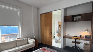 A hotel room with a bed, a sofa, a desk with a chair, and a view of the city through a window. - Ace Hotel Seattle (Seattle)