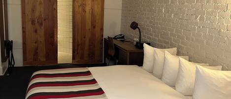A hotel room with a large bed, wooden sliding doors, a brick wall, and a desk with a lamp.