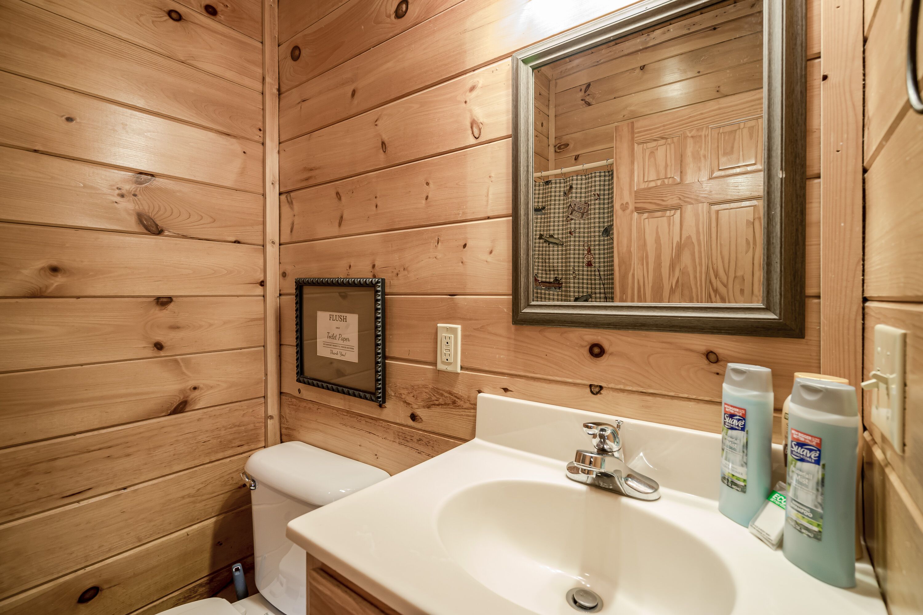 Un baño con paneles de madera, un inodoro, un lavamanos y un espejo.