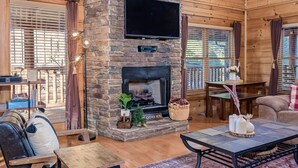 A cozy cabin interior with a stone fireplace, wooden furniture, and a television mounted on the wall. - Bear Vista Retreat w HotTub Pool View (Sevierville)