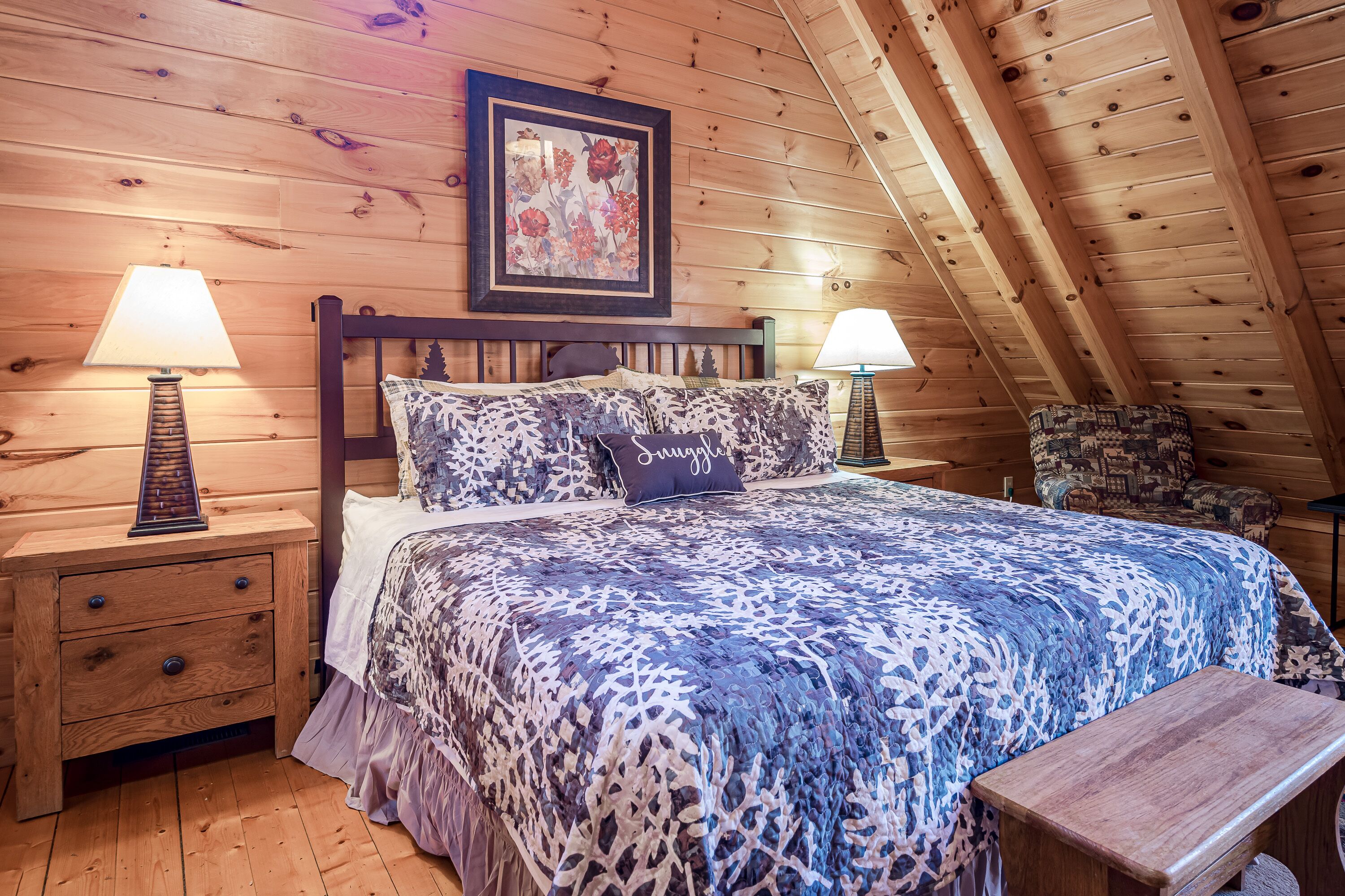 Una habitación con paneles de madera, una cama, dos mesitas de noche, una silla y un cuadro en la pared.